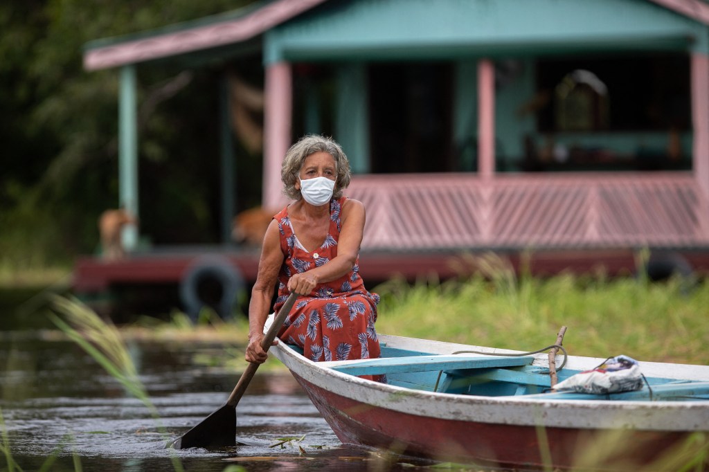 Olga D'arc Pimentel, 72, rows a boat to be vaccinated by a health worker with a dose of Oxford-AstraZeneca COVID-19 vaccine in the Nossa Senhora Livramento community on the banks of the Rio Negro near Manaus, Amazonas state, Brazil on February 9, 2021. (Photo by MICHAEL DANTAS / AFP)
