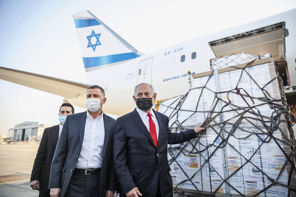EM CAMPANHA - Netanyahu (de máscara preta) recebe o primeiro lote de doses: triunfo político às vésperas da eleição -