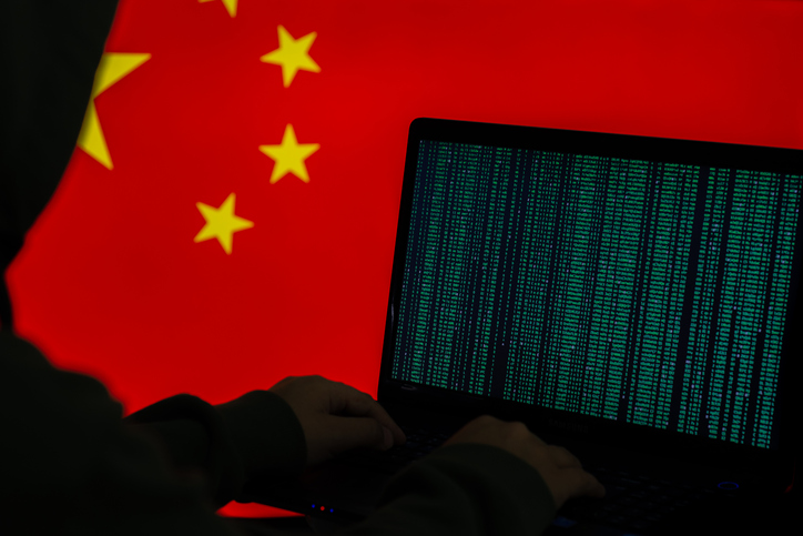Imagem em silhueta de uma pessoa teclando em um computador, com a bandeira chinesa ao fundo