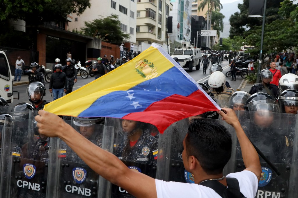 Manifestante segura bandeira da Venezuela ao lado de membros da tropa de choque da Polícia Nacional, em Caracas. 10/03/2020