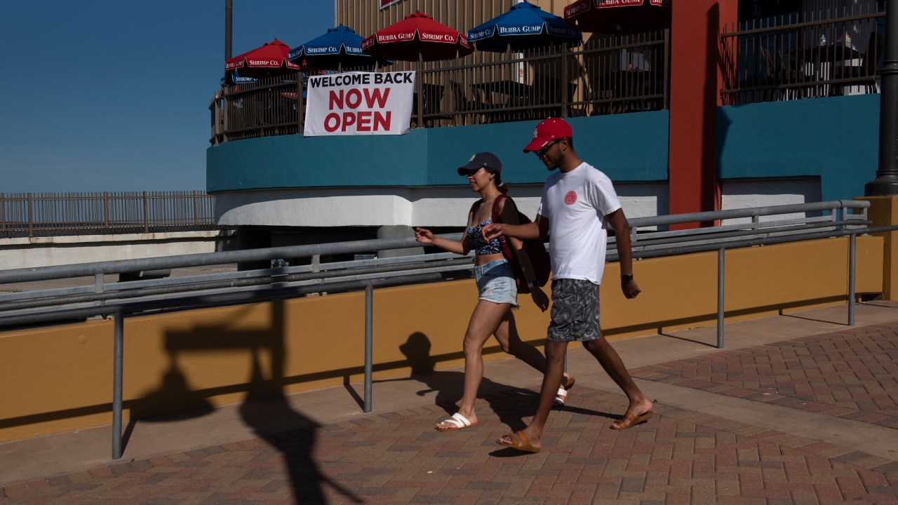 Pessoas caminham sem máscaras perto de estabelecido com placa "aberto" em Galveston, Texas. 01/05/2020
