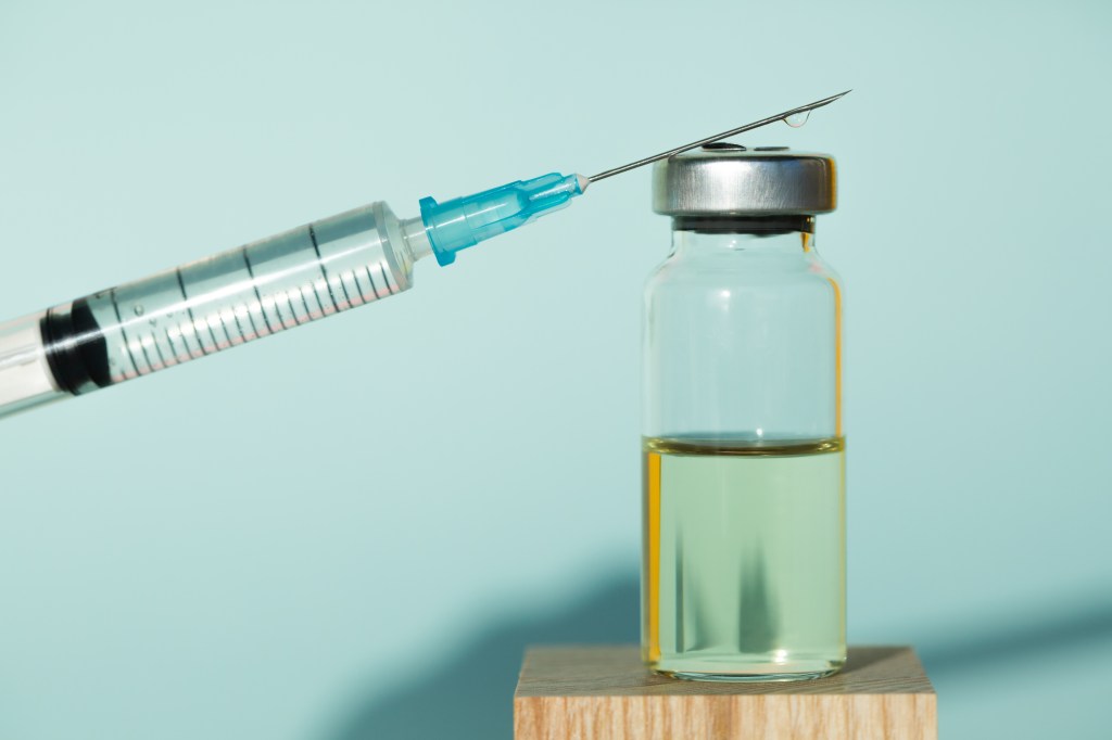 Clean syringe and sealed vial of liquid remedy placed on wooden cubes against blue background