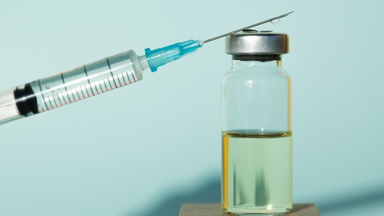 Clean syringe and sealed vial of liquid remedy placed on wooden cubes against blue background