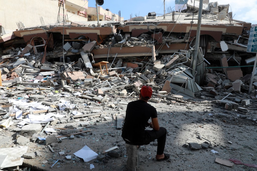 Homem palestino sentado nos destroços de prédio destruído por ataque aéreo israelense em Gaza. 18/05/2021