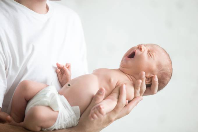 Male hands holding a screaming newborn