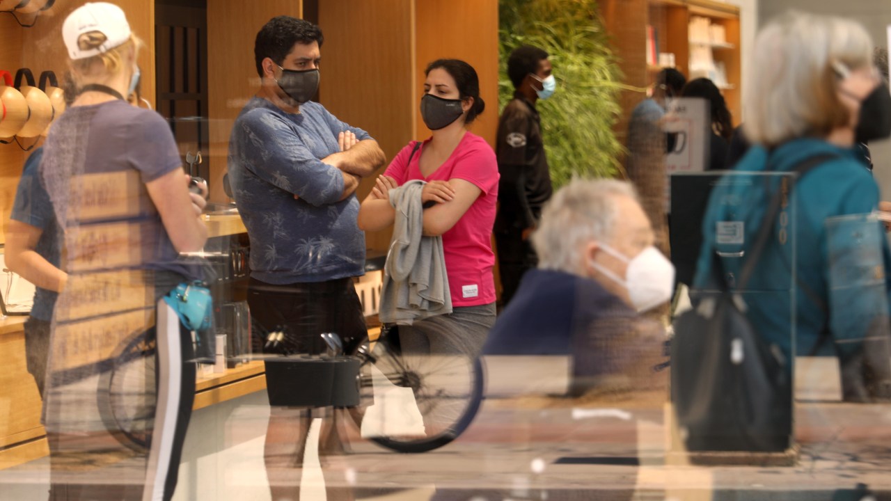SANTA MONICA, CA - MAY 14, 2021 - - Customers, masked against COVID-19, wait for service inside an Apple store on the Third Street Promenade a day after the CDC relaxed the use of wearing masks in Santa Monica on May 14, 2021. Californians are on stand by since the state has not relaxed its rules on mask wearing just yet. (Genaro Molina / Los Angeles Times via Getty Images)