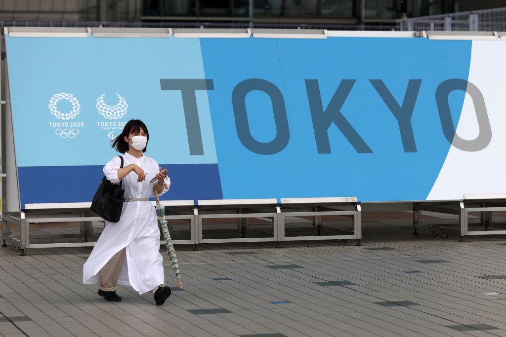 Mulher com máscara em frente a banner dos Jogos Olímpicos de Tóquio, na capital japonesa. 01/07/2021