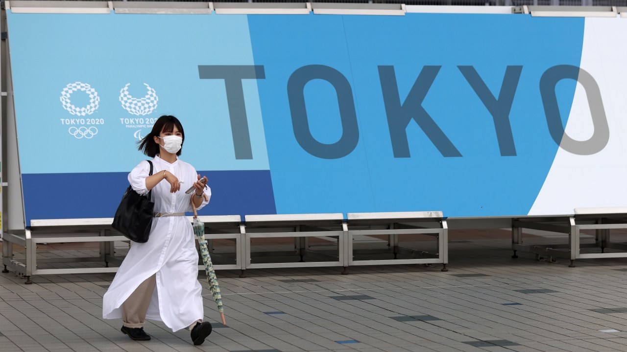 Mulher com máscara em frente a banner dos Jogos Olímpicos de Tóquio, na capital japonesa. 01/07/2021