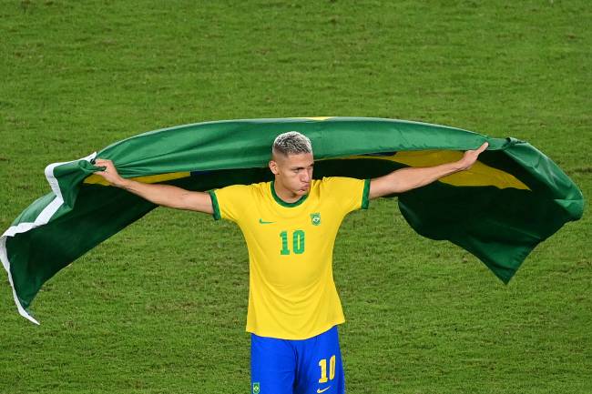 Brazil's Richarlison, with a Brazilian flag, celebrates after winning the Tokyo 2020 Olympic Games football competition men's gold medal match by defeating Spain 2-1 in extra time at Yokohama International Stadium in Yokohama, Japan, on August 7, 2021. (Photo by Vincenzo PINTO / AFP)