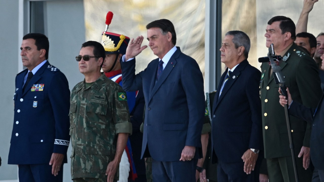 Brazilian President Jair Bolsonaro (C) smiles next to his Defense Minister Braga Netto (2R), Navy Commander Almir Garnier (L), during a military vehicles parade in front of the Planalto Palace in Brasilia, on August 10, 2021. - Bolsonaro is accused of using the armed forces for a show of force to intimidate National Congress, where a bill is being debated to modify the electronic voting system. (Photo by EVARISTO SA / AFP)