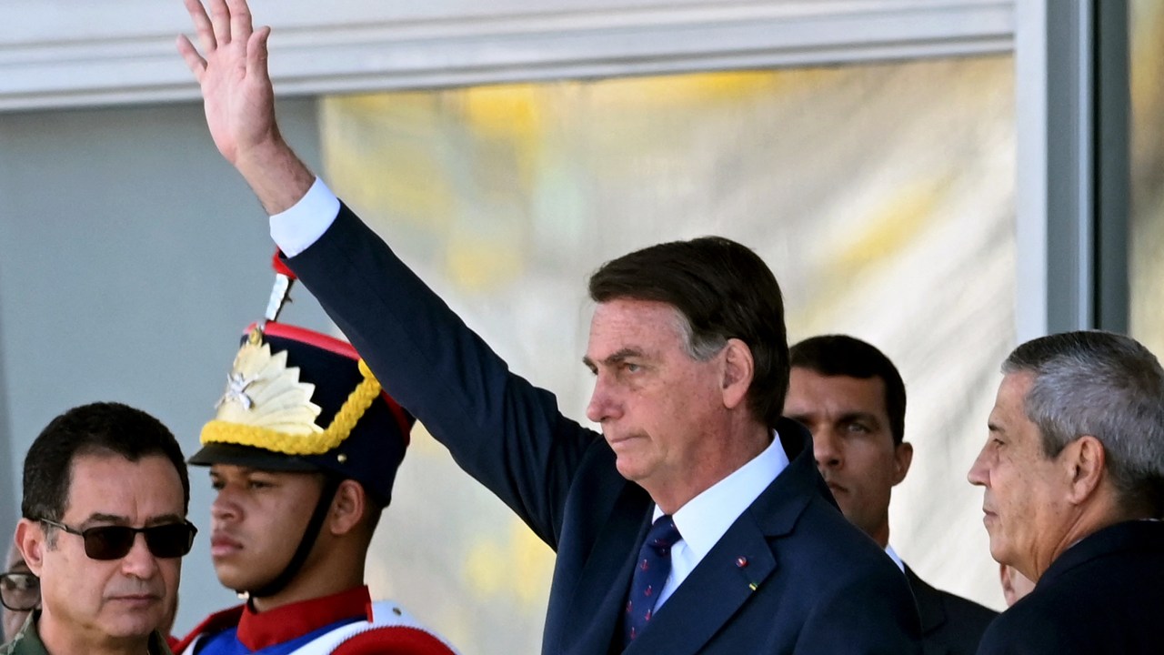 Brazilian President Jair Bolsonaro (C) waves next to his Defense Minister Braga Netto (R), and Navy Commander Almir Garnier (L), during a military vehicles parade in front of the Planalto Palace in Brasilia, on August 10, 2021. - Bolsonaro is accused of using the armed forces for a show of force to intimidate National Congress, where a bill is being debated to modify the electronic voting system. (Photo by EVARISTO SA / AFP)