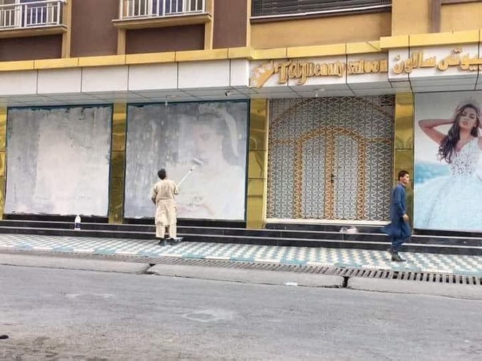 Funcionários cobrem fotos de mulheres na fachada de um salão de beleza em Cabul