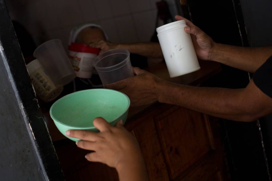 Voluntários com recipientes de plástico para enchê-los com comida para distribuir em uma igreja evangélica no centro da cidade de Caracas -