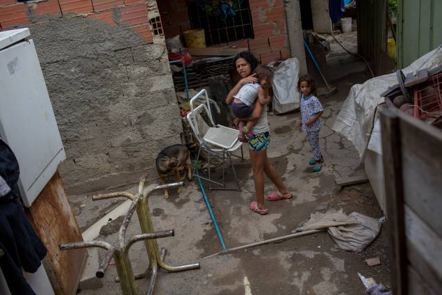 Mulher carregando sua filha de 2 anos dentro de uma favela do rio Guaire, em Caracas -