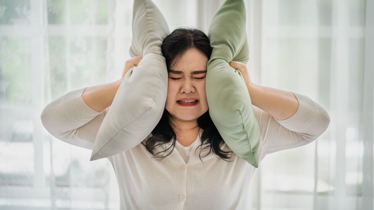 Woman covering her ears with a pillow, the concept does not want to hear things. affecting oneself