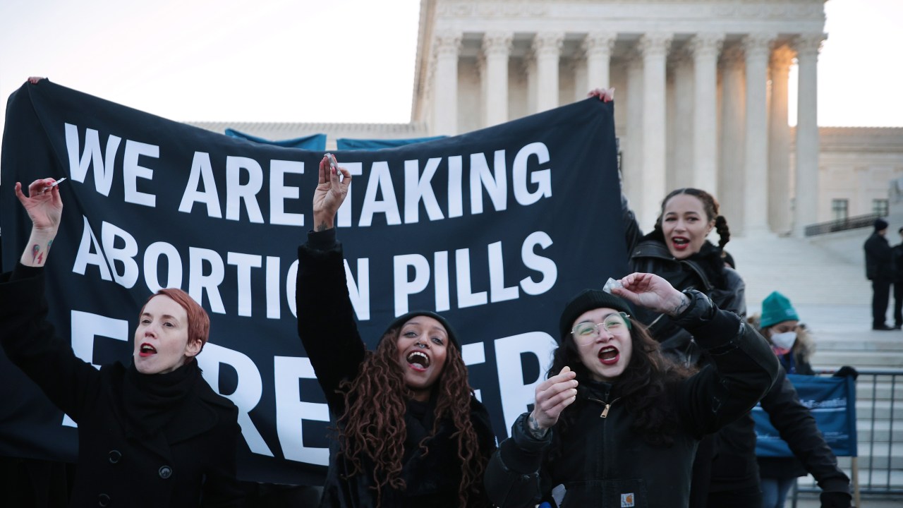 WASHINGTON, DC - DECEMBER 01: (L-R) Lila Bonow, Alana Edmondson and Aiyana Knauer prepare to take abortion pill while demonstrating in front of the U.S. Supreme Court as the justices hear hear arguments in Dobbs v. Jackson Women's Health, a case about a Mississippi law that bans most abortions after 15 weeks, on December 01, 2021 in Washington, DC. With the addition of conservative justices to the court by former President Donald Trump, experts believe this could be the most important abortion case in decades and could undermine or overturn Roe v. Wade. (Photo by Chip Somodevilla/Getty Images)