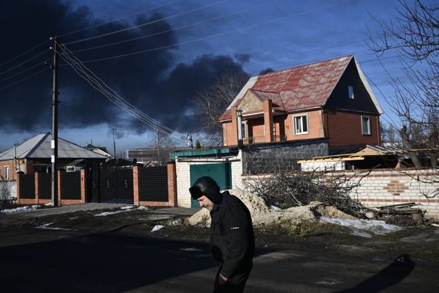 Um homem caminha em uma rua enquanto fumaça preta sobe de um aeroporto militar em Chuguyev, perto de Kharkiv -