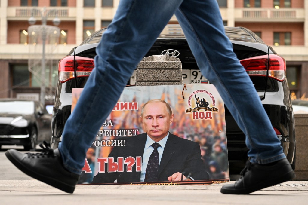A placard featuring an image of Russian President Vladimir Putin and reading "We are with him for the sovereignty of Russia! And you?" is seen left in front of the Russian State Duma building in central Moscow on February 24, 2022. - Russian President Vladimir Putin has launched a military operation in Ukraine after weeks of intense diplomacy and the imposition of Western sanctions on Russia that failed to deter him. (Photo by Kirill KUDRYAVTSEV / AFP)