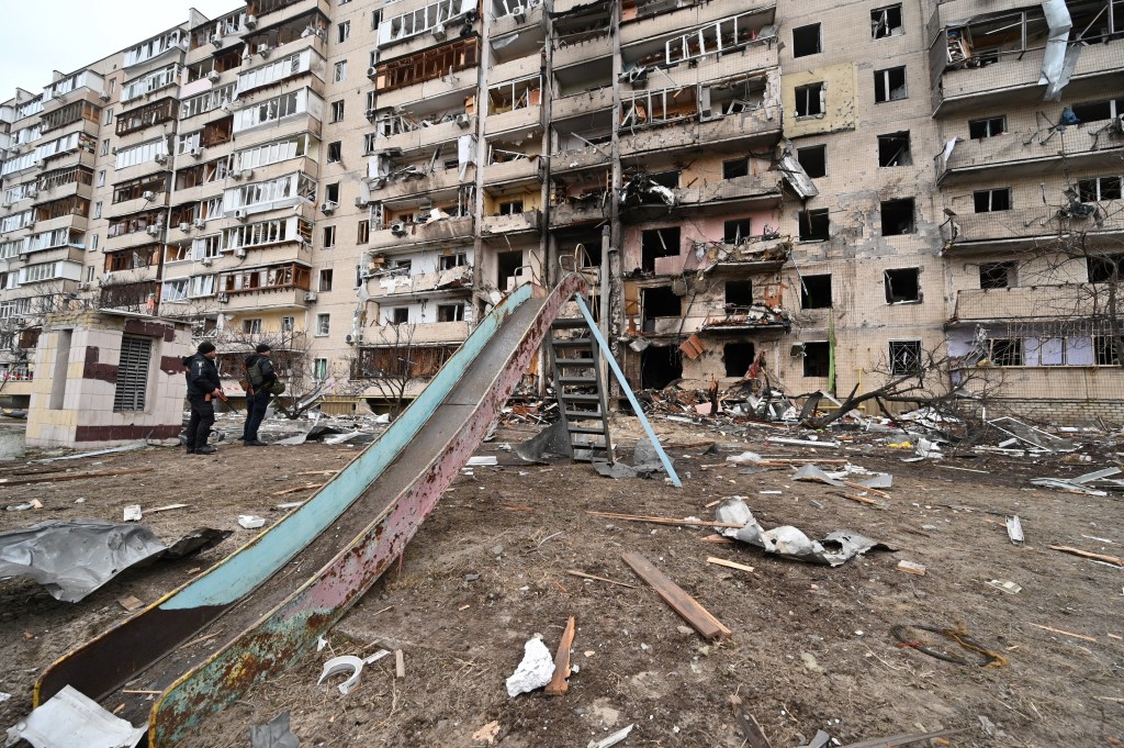 Police officers stand guard at a damaged residential building at Koshytsa Street, a suburb of the Ukrainian capital Kyiv, where a military shell allegedly hit, on February 25, 2022. - Invading Russian forces pressed deep into Ukraine as deadly battles reached the outskirts of Kyiv, with explosions heard in the capital early Friday that the besieged government described as "horrific rocket strikes". The blasts in Kyiv set off a second day of violence after Russian President Vladimir Putin defied Western warnings to unleash a full-scale ground invasion and air assault that quickly claimed dozens of lives and displaced at least 100,000 people. (Photo by GENYA SAVILOV / AFP)