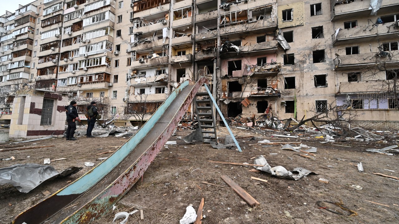 Police officers stand guard at a damaged residential building at Koshytsa Street, a suburb of the Ukrainian capital Kyiv, where a military shell allegedly hit, on February 25, 2022. - Invading Russian forces pressed deep into Ukraine as deadly battles reached the outskirts of Kyiv, with explosions heard in the capital early Friday that the besieged government described as "horrific rocket strikes". The blasts in Kyiv set off a second day of violence after Russian President Vladimir Putin defied Western warnings to unleash a full-scale ground invasion and air assault that quickly claimed dozens of lives and displaced at least 100,000 people. (Photo by GENYA SAVILOV / AFP)