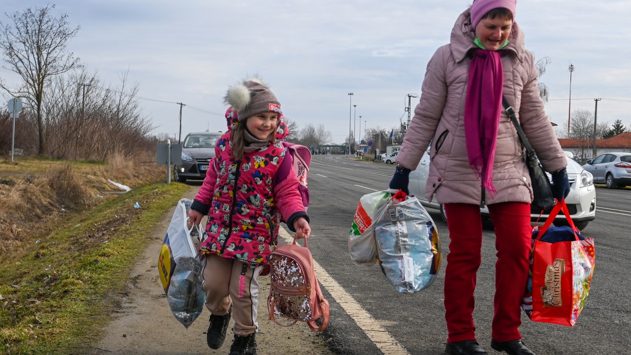 A Ukrainian mother walks with her daughter along the road from the Hungarian-Ukrainian border crossing near Beregsurany, Hungary, some 300 km from the Hungarian capital on February 25, 2022, as Ukrainian citizens have started to flee the conflict in their country one day after Russia launched a military attack on neighbouring Ukraine. - As Ukraine braces for a feared Russian invasion, its EU member neighbours are making preparations for a possible influx of hundreds of thousands or even millions of refugees fleeing military action. (Photo by ATTILA KISBENEDEK / AFP)