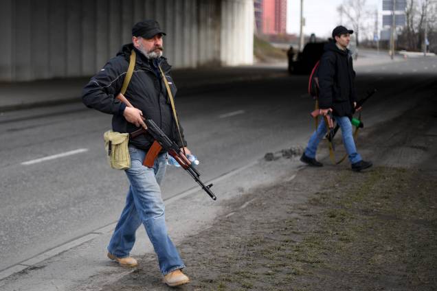 Voluntários, um segurando um fuzil AK-47, protegem uma estrada principal que leva a Kiev, na Ucrânia -