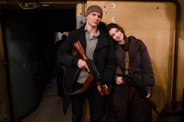 Um jovem casal que se junta aos combatentes da defesa territorial sorri depois de receber armas e munições em Kiev -