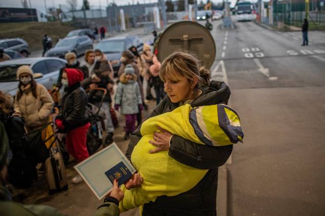 Uma mulher segura um bebê enquanto as pessoas esperam na fila na chegada à fronteira entre a Ucrânia e a Eslováquia -
