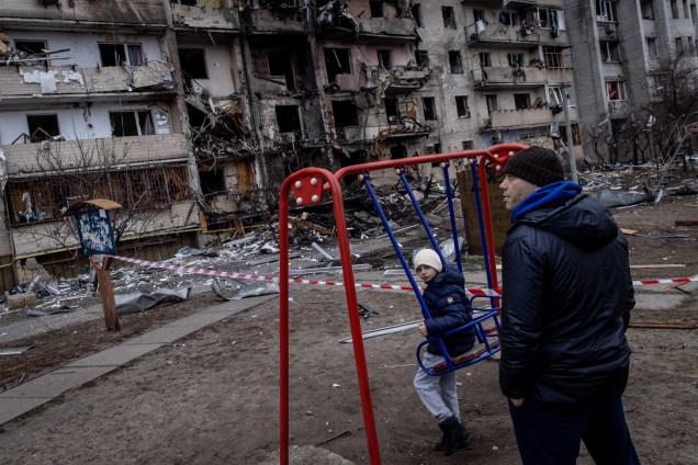 Ua criança brinca em um balanço em frente a um prédio residencial atingido por um ataque de mísseis -