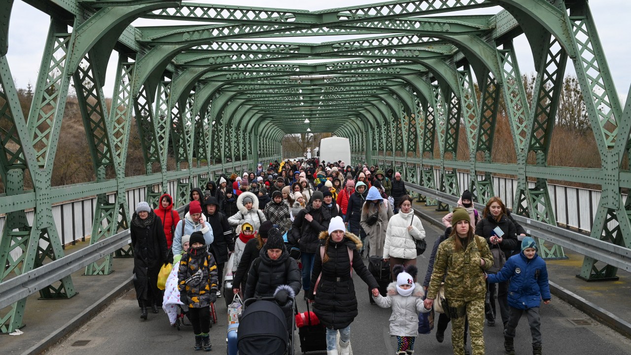 Ukrainian refugees walk a bridge at the buffer zone with the border with Poland in the border crossing of Zosin-Ustyluh, western Ukraine on March 6, 2022. - Over 1.5 million refugees have fled Ukraine in the week since the invasion by Russian on February 24, 2022, with over half going to Poland, according to the UN refugee agency. (Photo by Daniel LEAL / AFP)