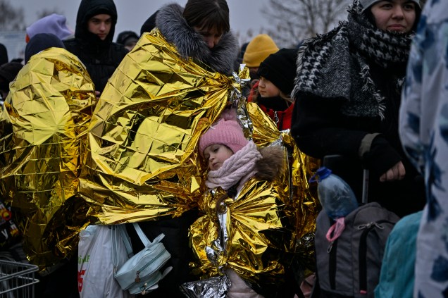 Pessoas esperam em temperaturas congelantes para serem transferidas para uma estação de trem depois de cruzar as fronteiras ucranianas para a Polônia -