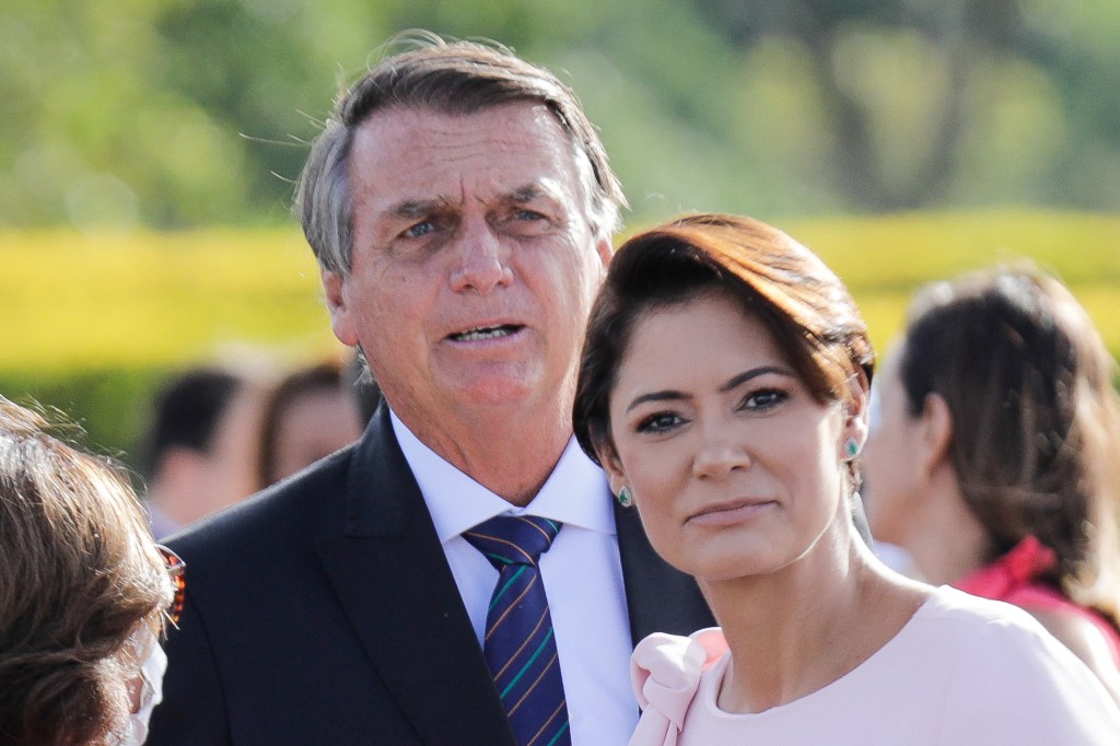 Brazilian President Jair Bolsonaro (L) participates in the flag-raising ceremony accompanied by his wife Michelle Bolsonaro on International Women's Day in front of the Alvorada Palace in Brasilia, on March 8, 2022. (Photo by Sergio Lima / AFP)