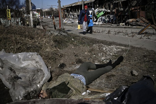 Moradores passam por um corpo de soldado russo enquanto evacuam a cidade de Irpin, na Ucrânia -