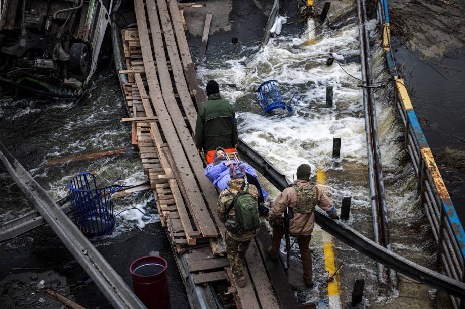 Militares ucranianos carregam uma idosa em uma maca em um caminho improvisado para atravessar um rio próximo a uma ponte destruída enquanto as pessoas fogem da cidade de Irpin, a noroeste de Kiev -