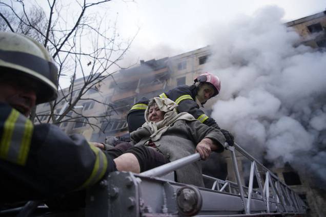bombeiros retiram uma idosa de um prédio de apartamentos atingido por bombardeios no distrito de Obolon, em Kiev -
