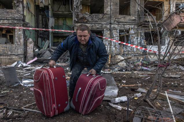Um homem carrega bagagem do edifício residencial atingido pelo bombardeio da artilharia russa, em Kiev -