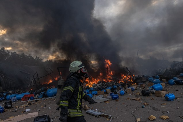 Um bombeiro ucraniano em ação tentando apagar o fogo no depósito com produtos químicos atingidos por bombardeios russos, nos arredores de Brovary -