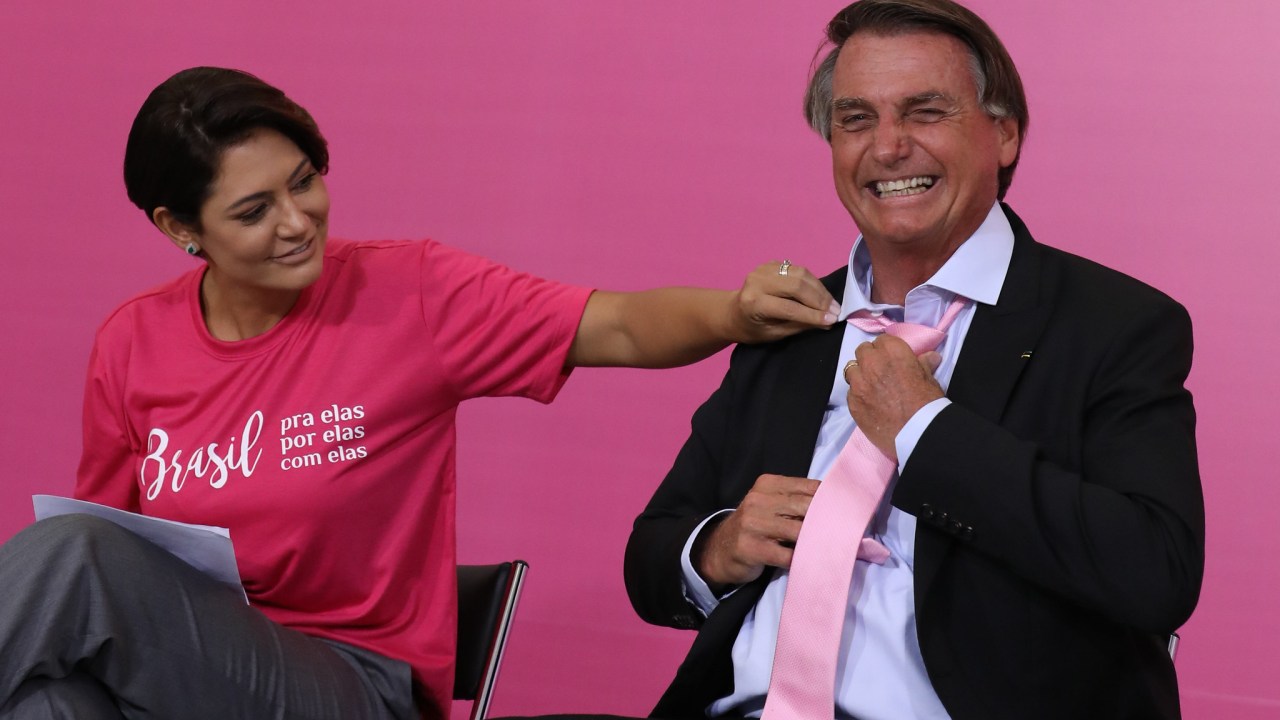 A primeira-dama Michelle Bolsonaro tenta arrumar gravata do presidente Jair Bolsonaro em evento do Dia Internacional da Mulher no Palácio do Planalto