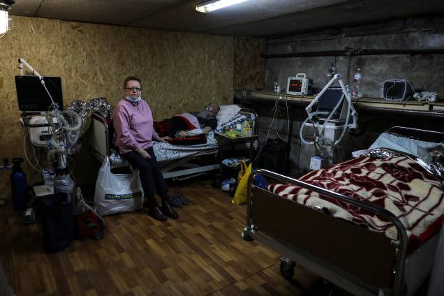 Olena Makukh sentada ao lado de seu marido Vilaty Makukhis, que está em tratamento de covid-19 desde 16 de fevereiro e agora está no abrigo subterrâneo do Hospital Zhytomyr, na Ucrânia -