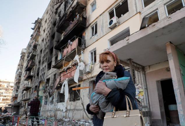 Uma mulher local carrega um gato ao deixar sua casa destruída após bombardeio em Kiev -
