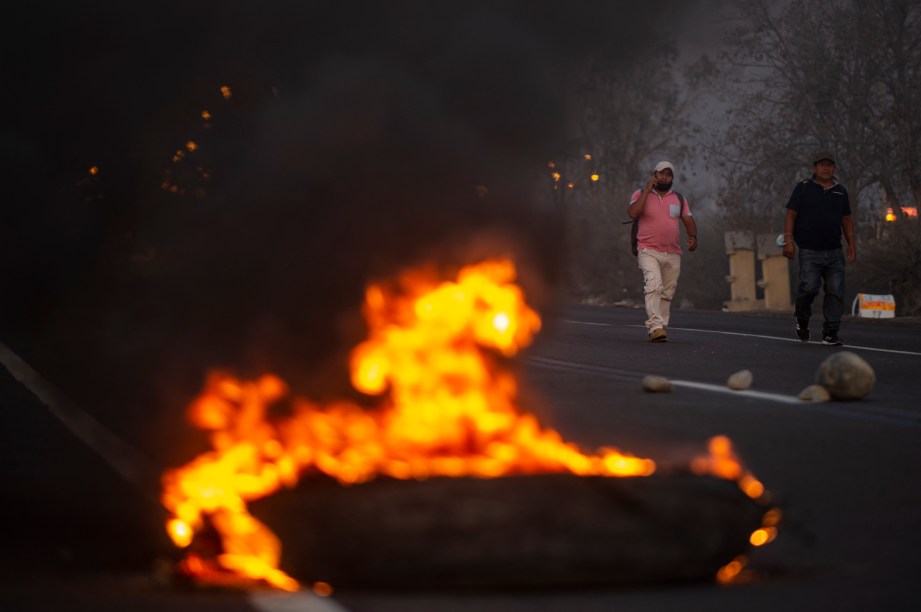 Homens caminham perto de pneus incendiados na rodovia Pan-Americana durante um bloqueio de estrada, em Ica, no sul do Peru -