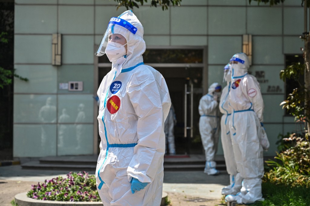 Workers and volunteers stand in a compound where residents are being tested for the Covid-19 coronavirus during the second stage of a pandemic lockdown in Jing' an district in Shanghai on April 6, 2022. (Photo by HECTOR RETAMAL / AFP)