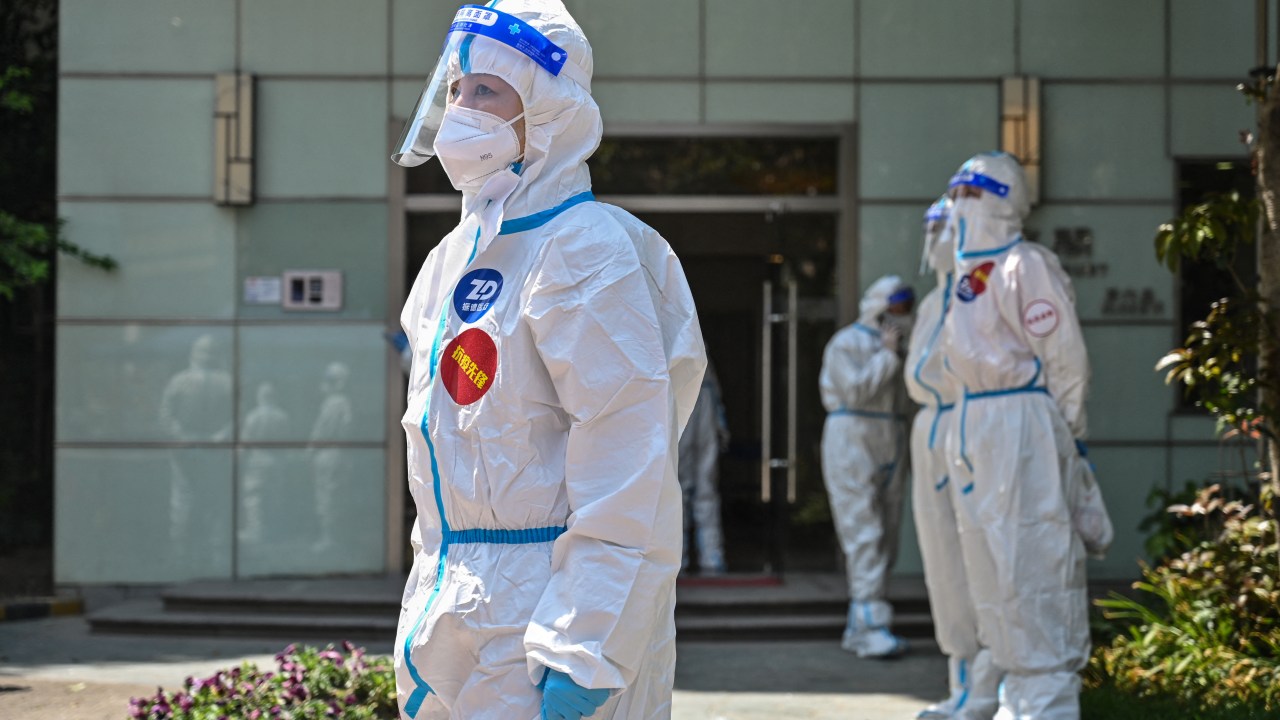 Workers and volunteers stand in a compound where residents are being tested for the Covid-19 coronavirus during the second stage of a pandemic lockdown in Jing' an district in Shanghai on April 6, 2022. (Photo by HECTOR RETAMAL / AFP)