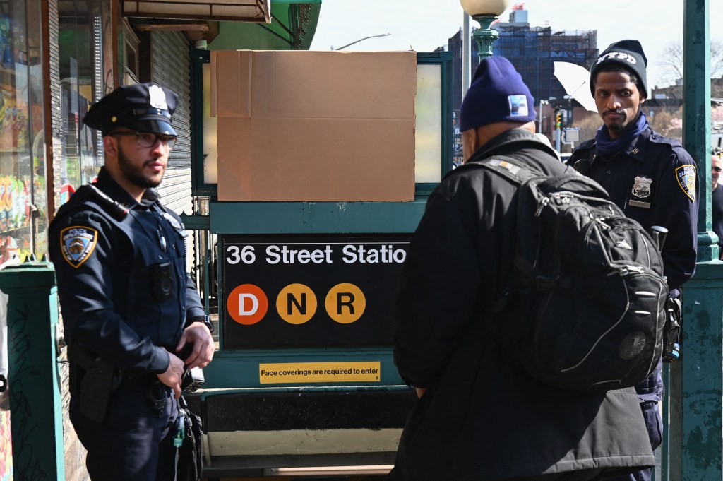 Police stand near a subway station in New York City on April 13, 2022, one day after people were injured during a rush-hour shooting in the Brooklyn borough of New York. - Nervous New York commuters crowded on to the subway Wednesday morning, as police on the streets above intensified their hunt for a fugitive gunman who shot 10 people in a train car the day before. Tuesday's incident in Brooklyn -- in which no one was killed -- was not being investigated as an act of terrorism, and none of the injuries were considered life threatening. Police have identified 62-year-old Frank James as a suspect in the attack, which also wounded 13 others as they scrambled to get out of the station or suffered smoke inhalation. (Photo by Angela Weiss / AFP)