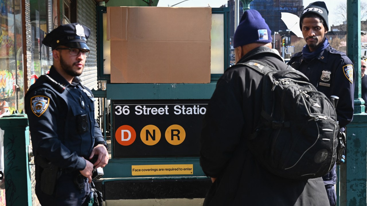 Police stand near a subway station in New York City on April 13, 2022, one day after people were injured during a rush-hour shooting in the Brooklyn borough of New York. - Nervous New York commuters crowded on to the subway Wednesday morning, as police on the streets above intensified their hunt for a fugitive gunman who shot 10 people in a train car the day before. Tuesday's incident in Brooklyn -- in which no one was killed -- was not being investigated as an act of terrorism, and none of the injuries were considered life threatening. Police have identified 62-year-old Frank James as a suspect in the attack, which also wounded 13 others as they scrambled to get out of the station or suffered smoke inhalation. (Photo by Angela Weiss / AFP)