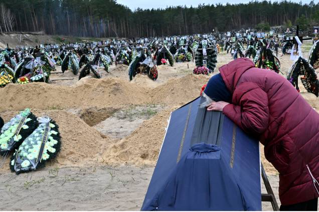 Uma mulher reage ao lado do caixão de seu marido durante um funeral em um cemitério em Irpin em 19 de abril de 2022. -