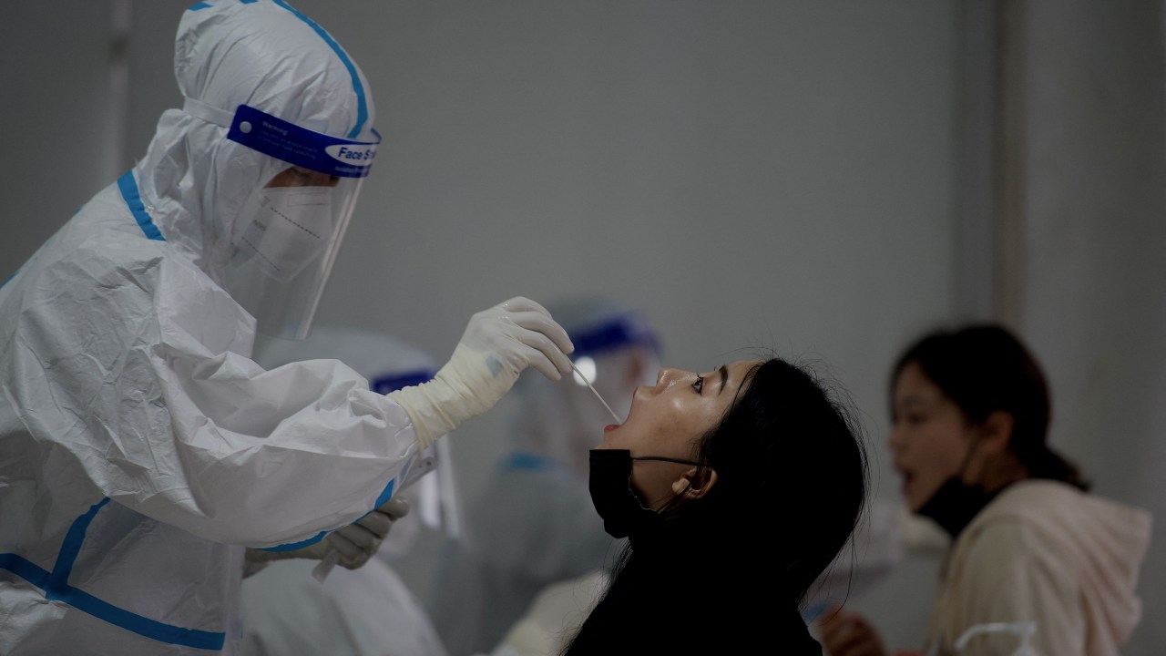 Um profissional de saúde coleta amostra de swab em uma mulher para ser testada para o coronavírus Covid-19 em um local de coleta de swab ao longo de uma rua em Pequim, em 25 de abril de 2022. (Foto de Noel Celis / AFP)