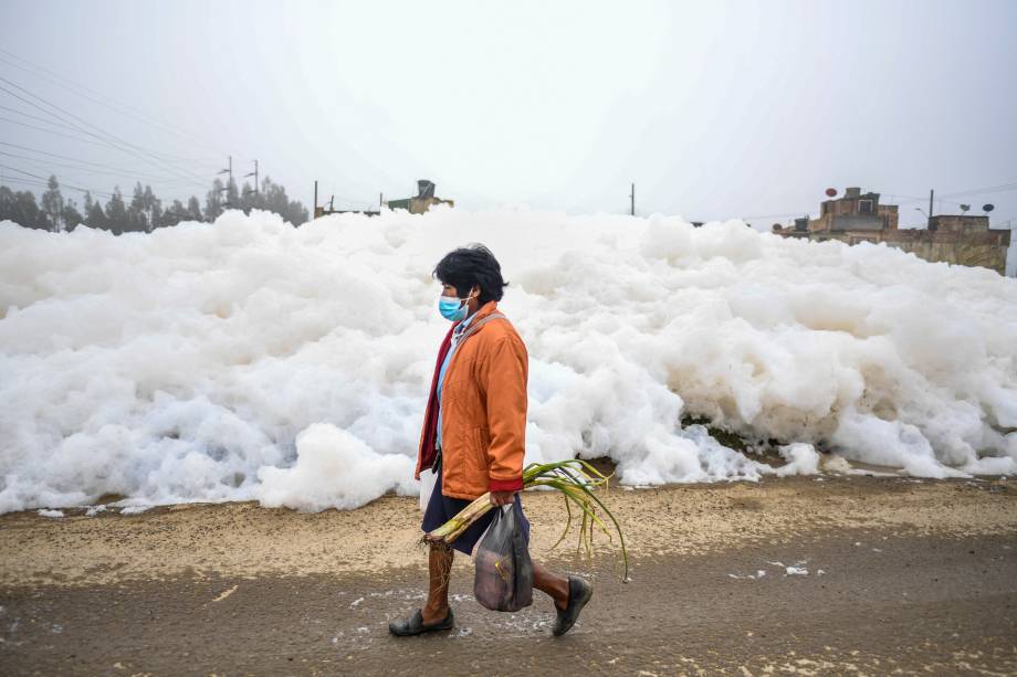 Uma mulher passa por uma parede de espuma que se formou em um rio poluído e invadiu o bairro de Los Puentes, em Mosquera, a oeste de Bogotá, em 26 de abril de 2022.