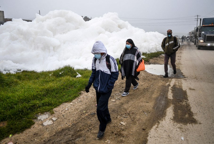 Pessoas caminham pela espuma pungente que se formou em um rio poluído e invadiu o bairro de Los Puentes, em Mosquera, a oeste de Bogotá, em 26 de abril de 2022