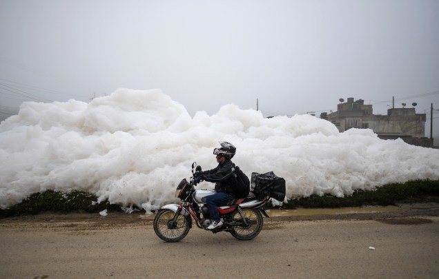 Um motociclista passa por uma espuma pungente que se formou em um rio poluído e invadiu o bairro de Los Puentes, em Mosquera, a oeste de Bogotá, em 26 de abril de 2022.